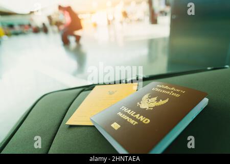 Thailand passport and vaccine passport on baggage on blur background of tourist in the airport. Certificate of vaccination for travel during coronavirus outbreak. Thai words are Thailand passport. Stock Photo