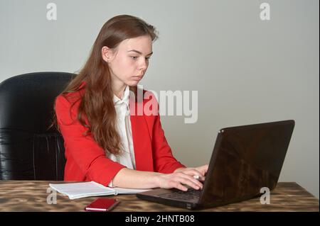 A woman sitting at a desk working with a laptop and notepad Stock Photo