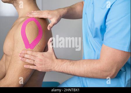 Physical therapist applying kinesio tape on male patient shoulder. Kinesiology, physical therapy, rehabilitation concept. close up Stock Photo