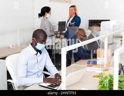 Company employee IT in a protective mask works behind laptop in an office Stock Photo