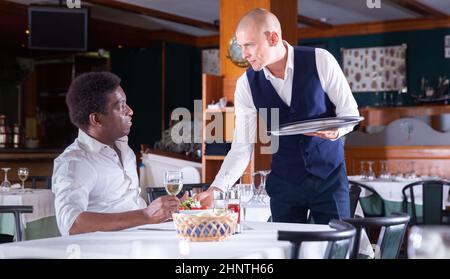 positive waitress bringing order to male client in cafe Stock Photo