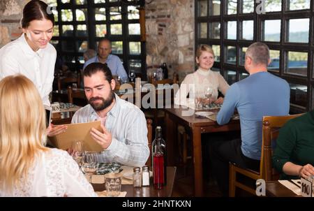 Guests of the country restaurant discuss menu with waitress Stock Photo