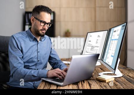 Looking At Invoice And Spreadsheet On Computer At Work Stock Photo