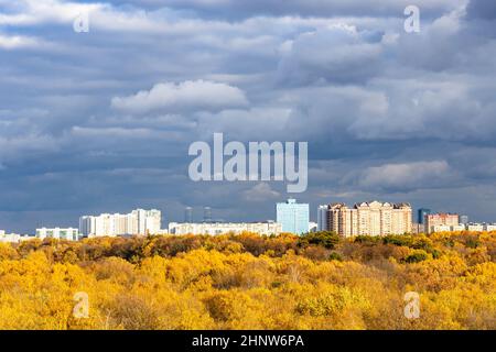 modern urban houses and yellow city park illuminated by sun under dark gray rainy clouds in sky on autumn day before rain Stock Photo
