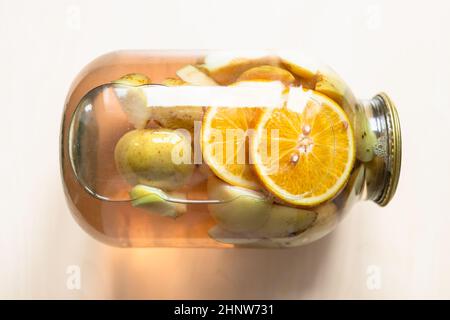 top view of lying 3-liter glass jar of homemade compote made from sliced fresh apples and oranges on light brown table Stock Photo