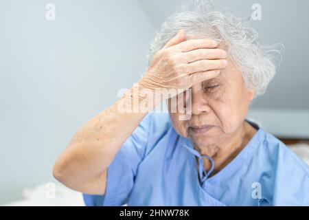 Asian senior or elderly old lady woman patient headache while sitting on bed in nursing hospital ward, healthy strong medical concept Stock Photo