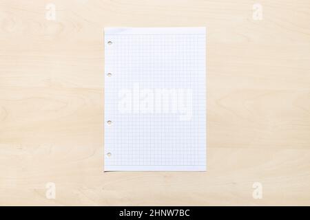top view of blank sheet of squared paper on light brown wooden board Stock Photo