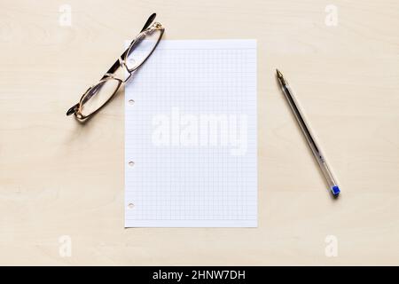top view of eyeglasses, pen and blank sheet of squared paper on light brown wooden board Stock Photo