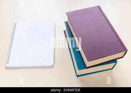 above view of two thick books and blank spiral notebook with squared paper on light brown wooden board Stock Photo