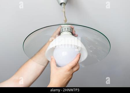 man replaces bulb of ceiling lamp at home Stock Photo
