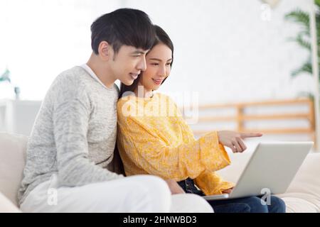 Young couple using laptop and watching video together in the living room. Stock Photo