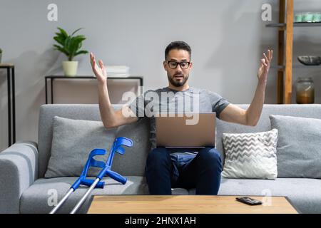 Injured Man With Broken Leg And Crutches Using Laptop Stock Photo