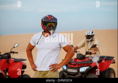 Two racers in helmets poses near atvs in desert Stock Photo - Alamy