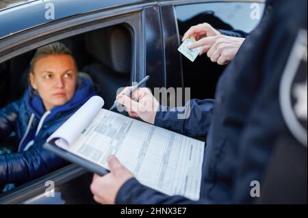 Police patrol checking driver's license of female driver. Policemen in uniform protect the law, registration of an offense. Cops work on city street, Stock Photo