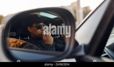 Male police officer in uniform and sunglasses talking on a walkie-talkie, view through the car rear view mirror. Policeman protect the law. Cop works Stock Photo