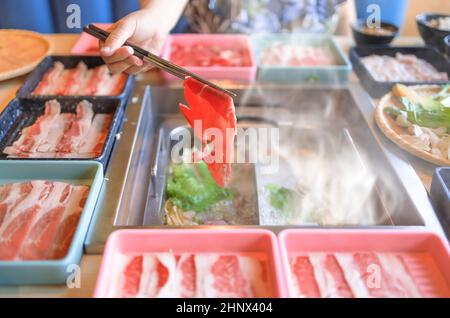 Chinese hot pot meal. Hands taking food with chopsticks. Stock Photo