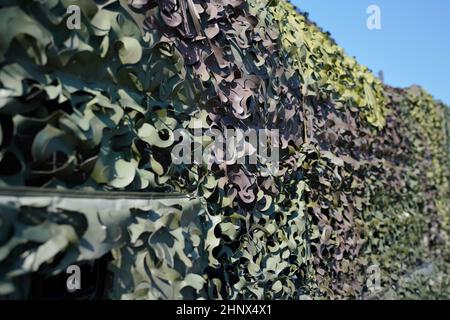Armoured military vehicle covered with camouflage fabric mesh, closeup detail. Stock Photo