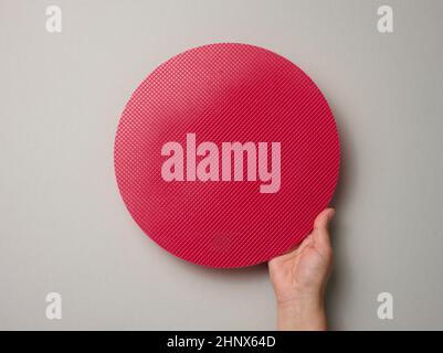 female hand holds empty red plastic textured cake plate on a gray background, top view Stock Photo