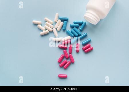 Various multicolored pills - blue, pink, white flying from an open plastic bottle, isolated on a light blue background Stock Photo