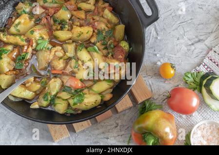 There are delicious zucchini fried with various vegetables on the table in a cast-iron frying pan. Top view, close-up. Stock Photo