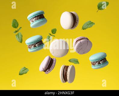 round baked macarons levitate on a yellow background, green mint leaves are flying around Stock Photo