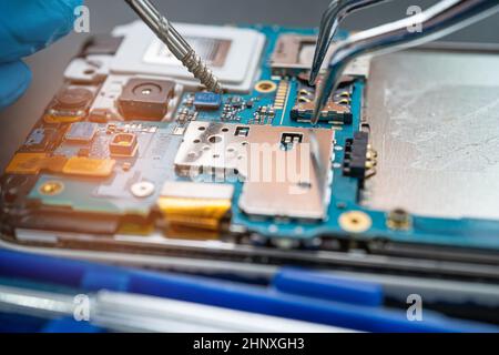 Technician repairing inside of mobile phone by soldering iron. Integrated Circuit. the concept of data, hardware, technology. Stock Photo