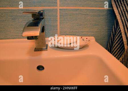 Modern faucet and classic soap dish on white basin. Stock Photo