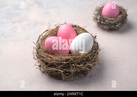 Three Easter eggs in a nest on a light background. Easter background. Side view, close-up. Stock Photo