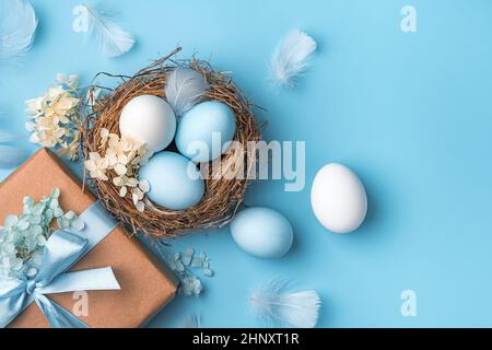 Easter pastel background with eggs, a nest and a gift on a blue background. The concept of a Happy Easter. Top view, copy space. Stock Photo