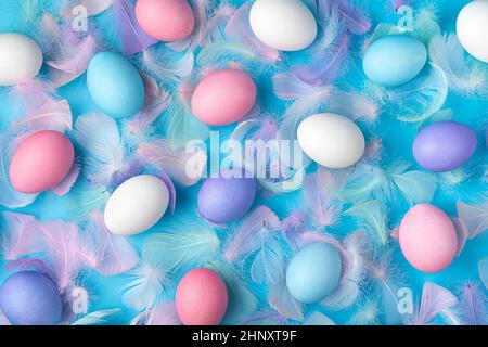 Colored Easter eggs and feathers on a blue background. Top view. Easter background. Stock Photo