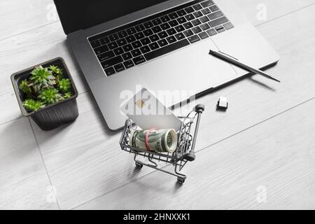 Online shopping concept. Shopping cart with dollars and credit card, laptop keyboard, flash drive, pen and houseplant. Stock Photo