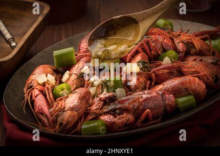 A close up of pouring melted butter on a platter of steamed crawfish and bits of peppers. Stock Photo