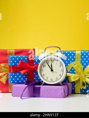 round alarm clock and a stack of gift boxes tied with a ribbon on a yellow background. Christmas and New Year Stock Photo