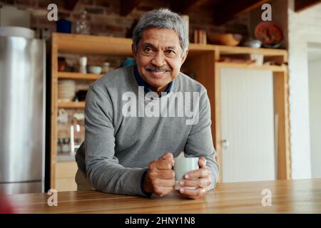 Portrait of retired biracial elderly male leaning on kitchen counter smiling at camera. Stock Photo