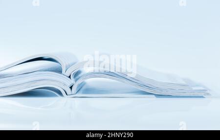 Stack of open magazines in blue tone on white background with copy space Stock Photo