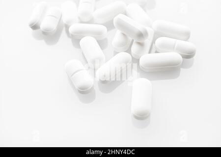 White medicine pills spilled on white background. Selective focus. Stock Photo
