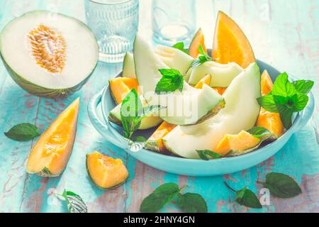 Healthy snack - Piel de sapo melon and cantaloupe with fresh mint on cyan wooden table Stock Photo