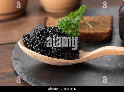 fresh grainy black paddlefish caviar in brown wooden spoon on a black background, close up Stock Photo