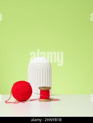 red ball with woolen thread and large needle on white table, green background Stock Photo