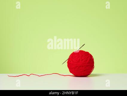 red ball with woolen thread on white table, green background Stock Photo