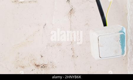 one white light switch in paint and putty is temporarily hanging on a black wire during repair against the background of an unfinished wall. open the Stock Photo