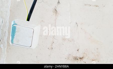 one white light switch in paint and putty is temporarily hanging on a black wire during repair against the background of an unfinished wall. open the Stock Photo
