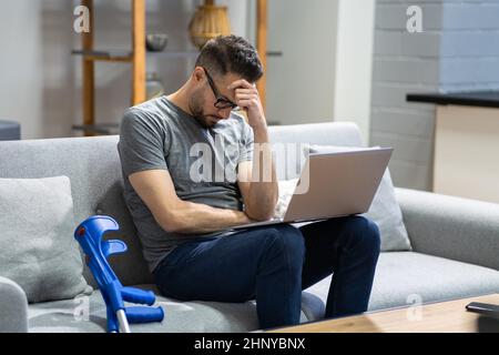 Injured Man With Broken Leg And Crutches Using Laptop Stock Photo