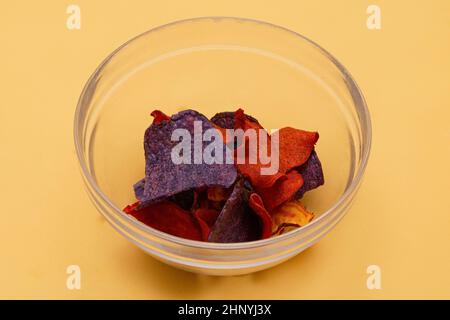 Colorful vegetables crisps pile made from sweet potato, blue potato and beetroot pile in transparent glass bowl Stock Photo