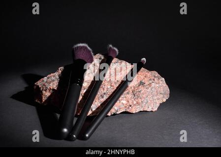 Makeup cosmetic brushes lie on granite stone on black background. Set of different cosmetic brushes for makeup artist. Stock Photo
