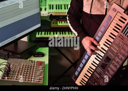 The musician plays the synthesizer in the small home studio while creating and recording electronic music. Stock Photo