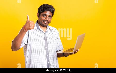 Asian happy portrait young black man smiling standing wear shirt using laptop computer and showing thumb up looking to camera isolated, studio shot ye Stock Photo