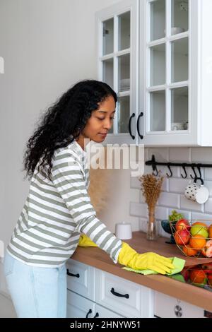 African-american woman occupied with household duties in kitchen. Wearing yellow rubber gloves Stock Photo