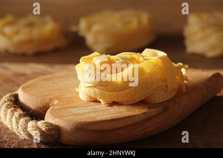 Raw italian pasta tagliatelle on wooden cutting board . Stock Photo