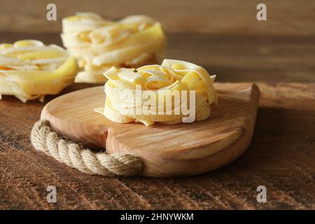 Raw italian pasta tagliatelle on wooden cutting board . Stock Photo